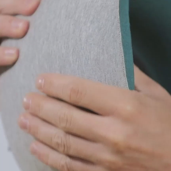 A man squeezing the Ostrichpillow Go Neck Pillow in Blue Reef, showing the responsive memory foam and how it rolls tightly for travel packability.