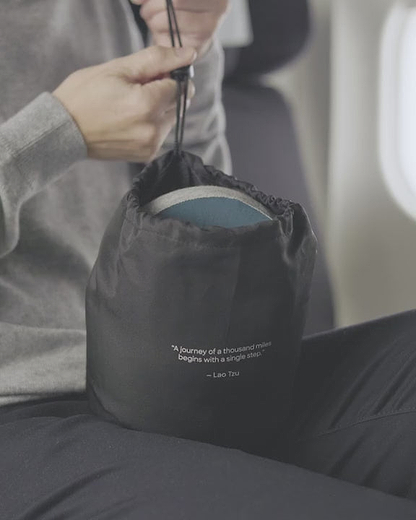 A person packing away the compressed Ostrichpillow Go Neck Pillow. It effortlessly compresses to reduce its volume by up to 60% for travel.