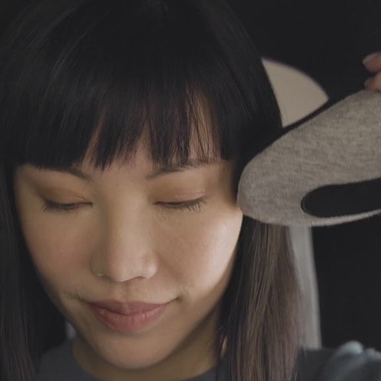 A woman wrapping a Deep Blue Go Neck Pillow around her neck. She fastens it securely and smiles as the memory foam travel pillow supports her head.