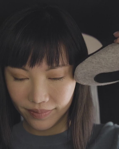 A woman wrapping a Deep Blue Go Neck Pillow around her neck. She fastens it securely and smiles as the memory foam travel pillow supports her head.