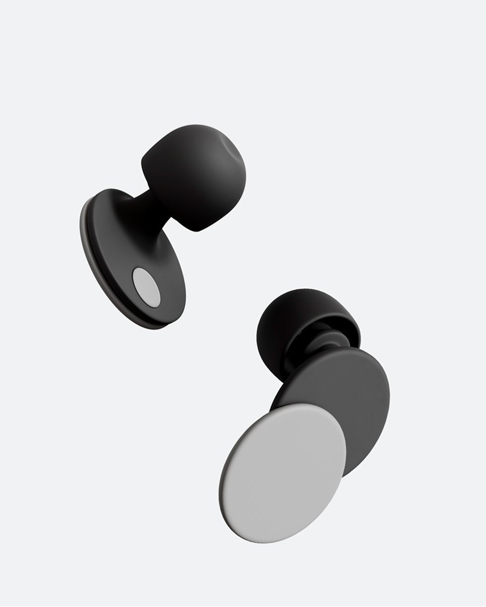 A woman resting her head back in an airplane seat. She wears Orbit Earplugs in the color Midnight Grey.