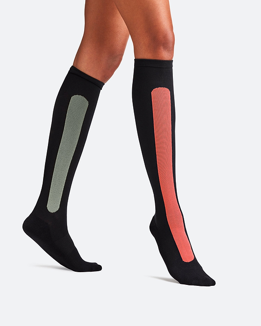 A traveler wearing Bamboo Compression Socks in the 'Sunset Red Olive Green' colorway, showing a prominent red stripe above the ankle.