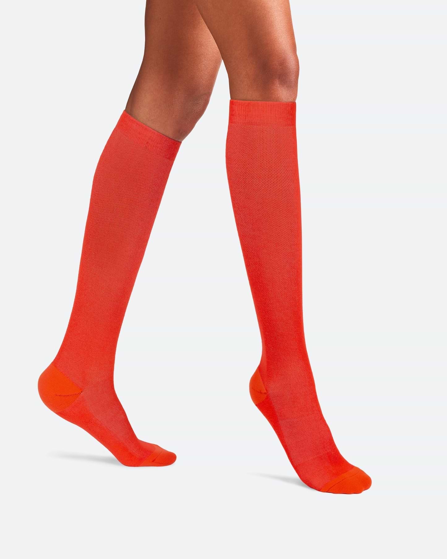 Side-profile view of a person's legs walking, wearing knee-high Ostrichpillow Bamboo Compression Socks in solid Sunset Red.