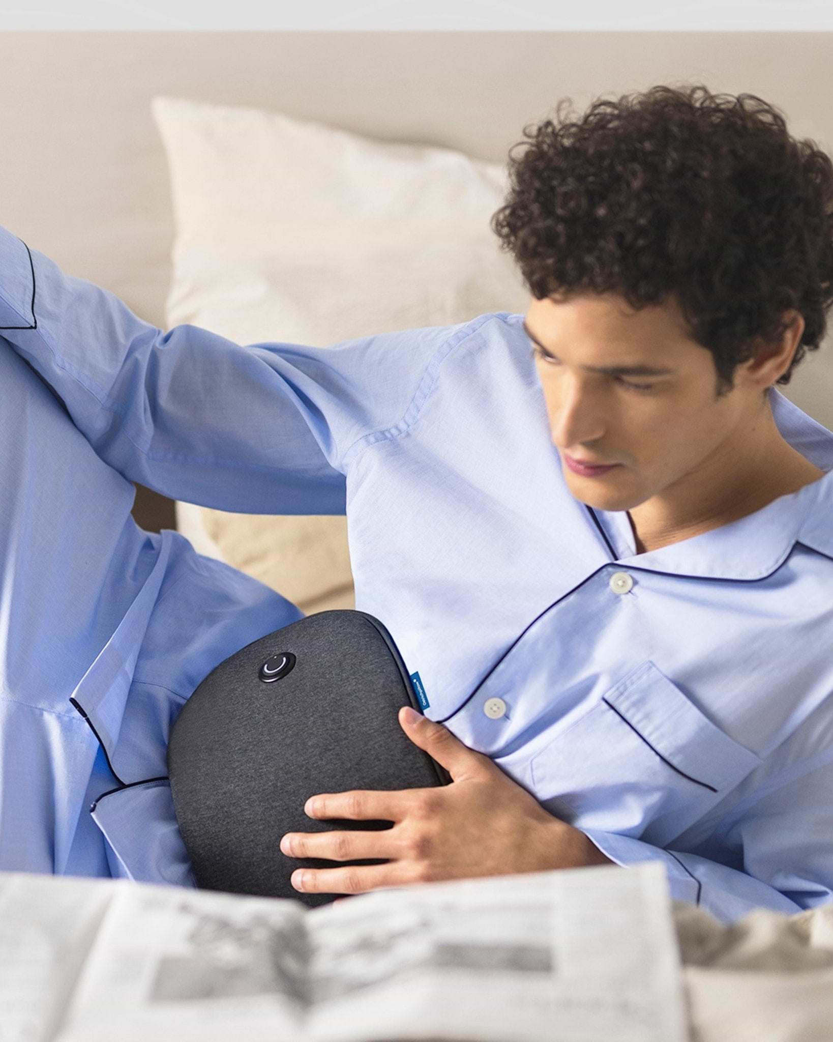 A man sitting back in bed pressing the soft, ergonomic Embrace Heating Pad to his stomach for heat therapy relaxation.
