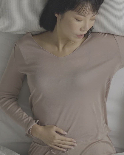 A woman lying in bed places Heatbag onto her lower abdomen, gently resting her hands over it for soothing warmth and comfort.