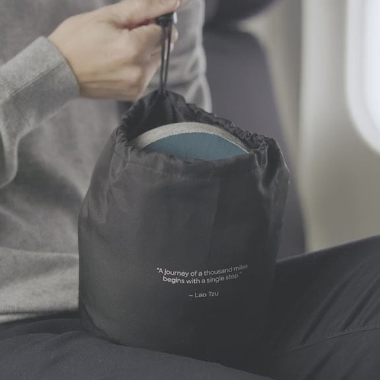 A person packing away the compressed Ostrichpillow Go Neck Pillow. It effortlessly compresses to reduce its volume by up to 60% for travel.