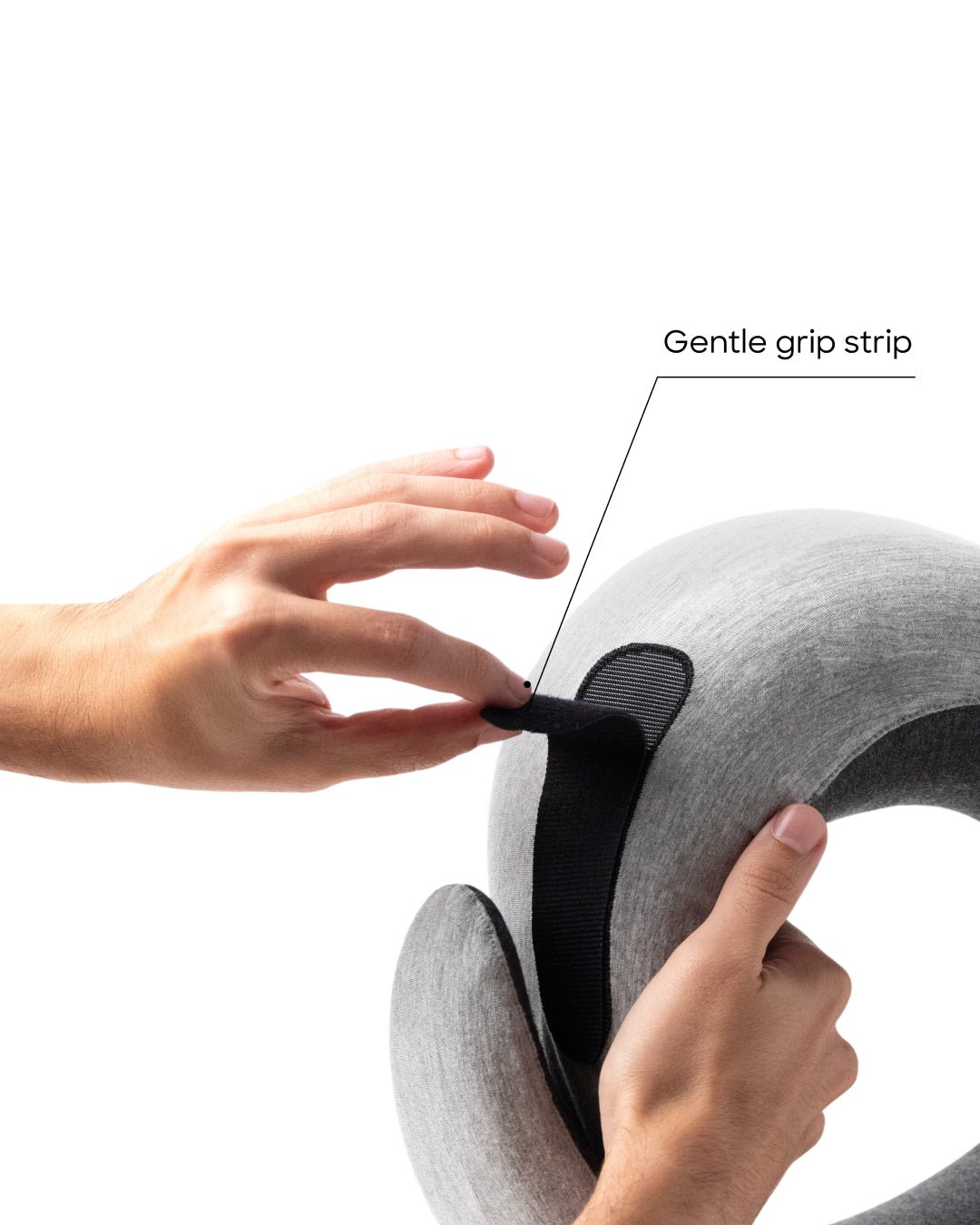A hand peeling back the adjustable fastening tab for the Ostrichpillow Go Neck Pillow in the color Midnight Grey and show its gentle grip strip.
