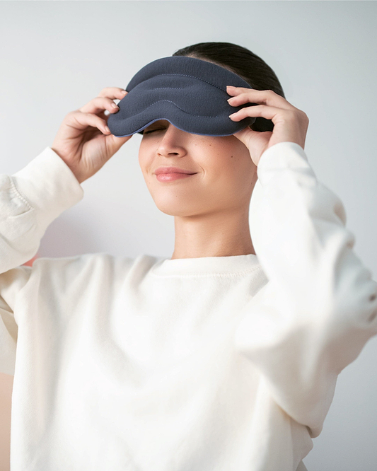 Woman prepares to rest with the Ostrichpillow Hot & Cold Eye Mask to relieve eye strain and promote relaxation.