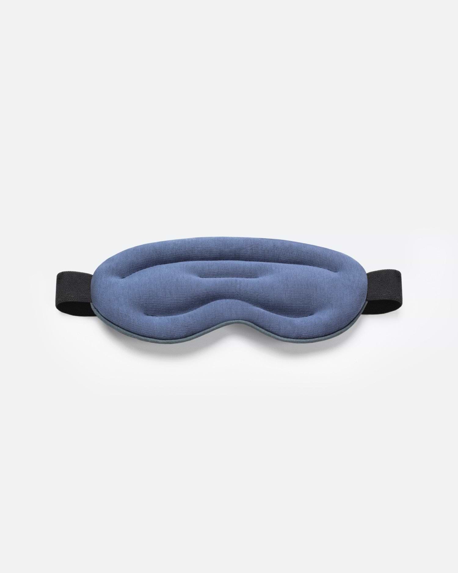 Top-down studio shot of a blue, ergonomically contoured Ostrichpillow Hot and Cold Eye Mask with a black elastic strap on a plain white background.