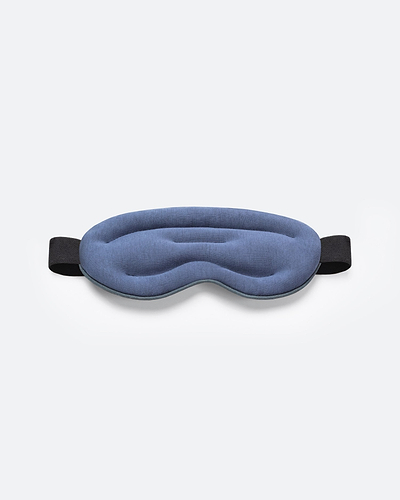 Top-down studio shot of a blue, ergonomically contoured Ostrichpillow Hot and Cold Eye Mask with a black elastic strap on a plain white background.
