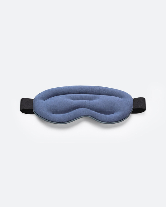 Top-down studio shot of a blue, ergonomically contoured Ostrichpillow Hot and Cold Eye Mask with a black elastic strap on a plain white background.