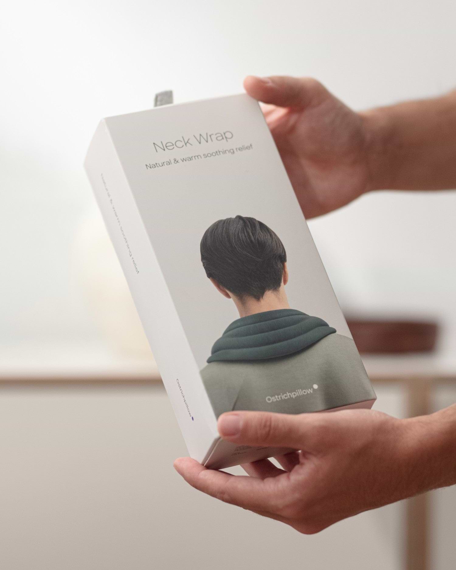 Close-up lifestyle and e-commerce packaging shot for the Heated Neck Wrap. A person holds the tall, rectangular white box.