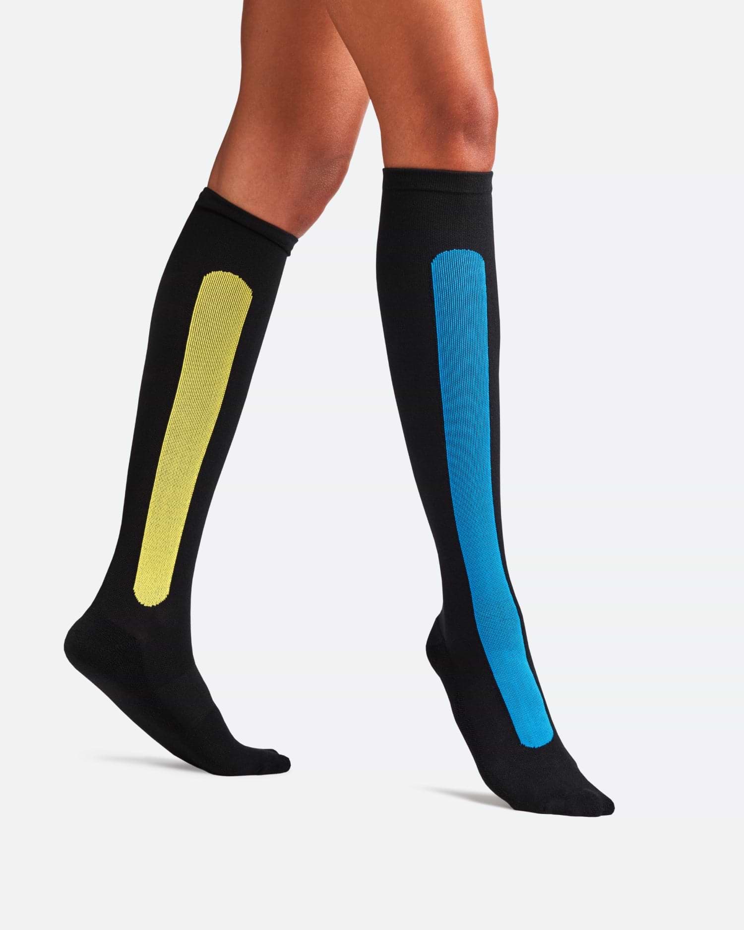 Side-profile view of a person walking, wearing knee-high Bamboo Compression Socks in the black and teal Blue Reef Caribbean Green colorway.