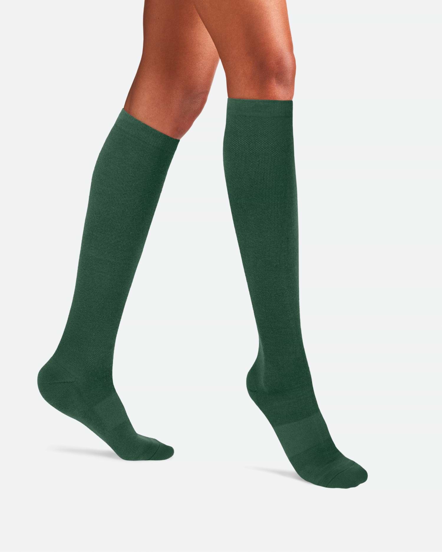Side-profile view of a person's legs walking, wearing knee-high Ostrichpillow Bamboo Compression Socks in solid Forest Green.