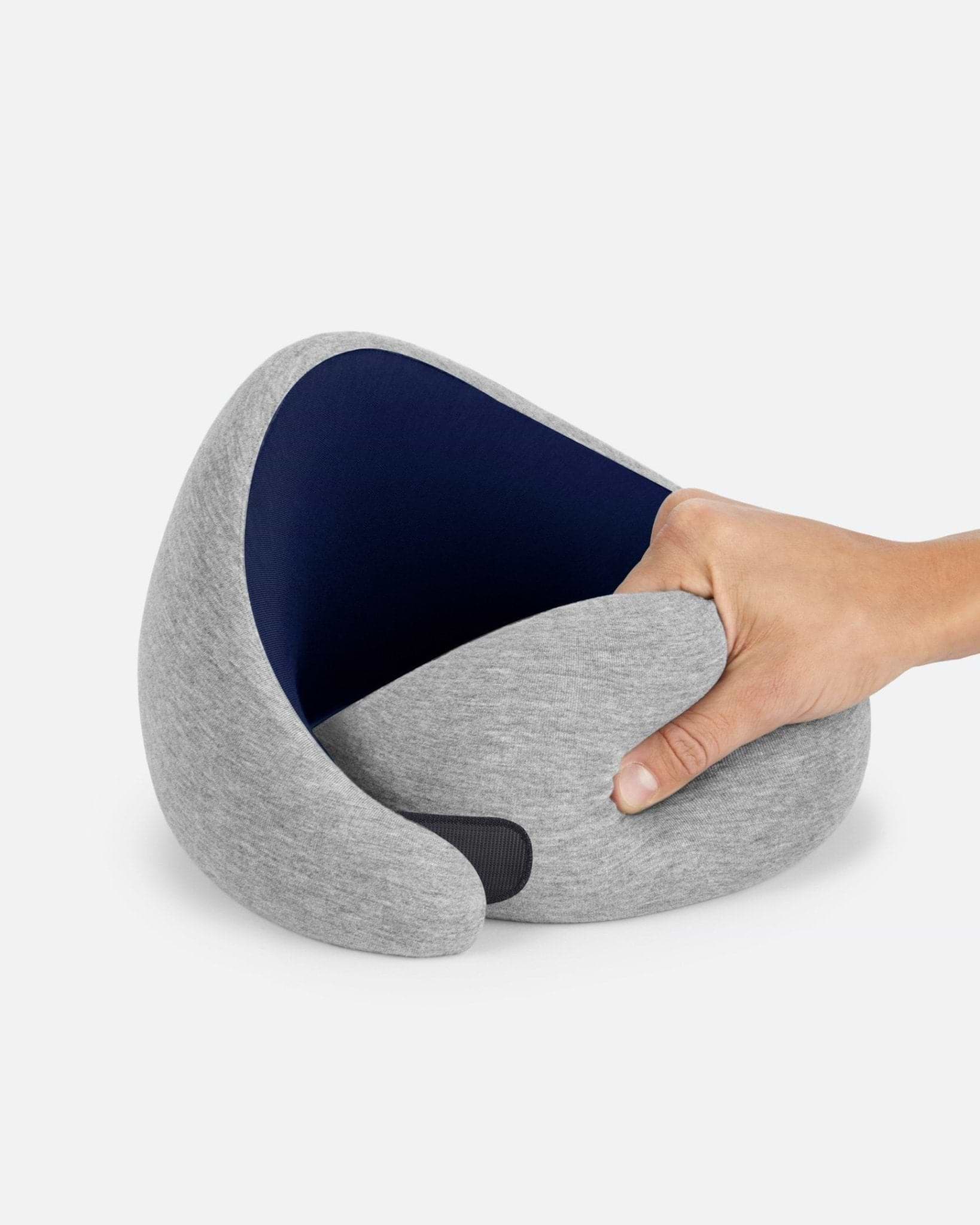 The Go Neck Pillow in Deep Blue showing its memory foam flexibility, with a light heather grey exterior and dark navy inner lining.