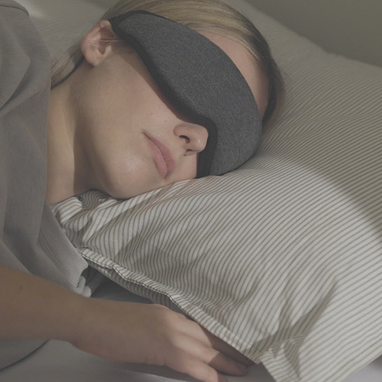 A woman rests with a dark grey Eye Mask. She smiles and text appears on screen that reads: 'Wake up refreshed'.