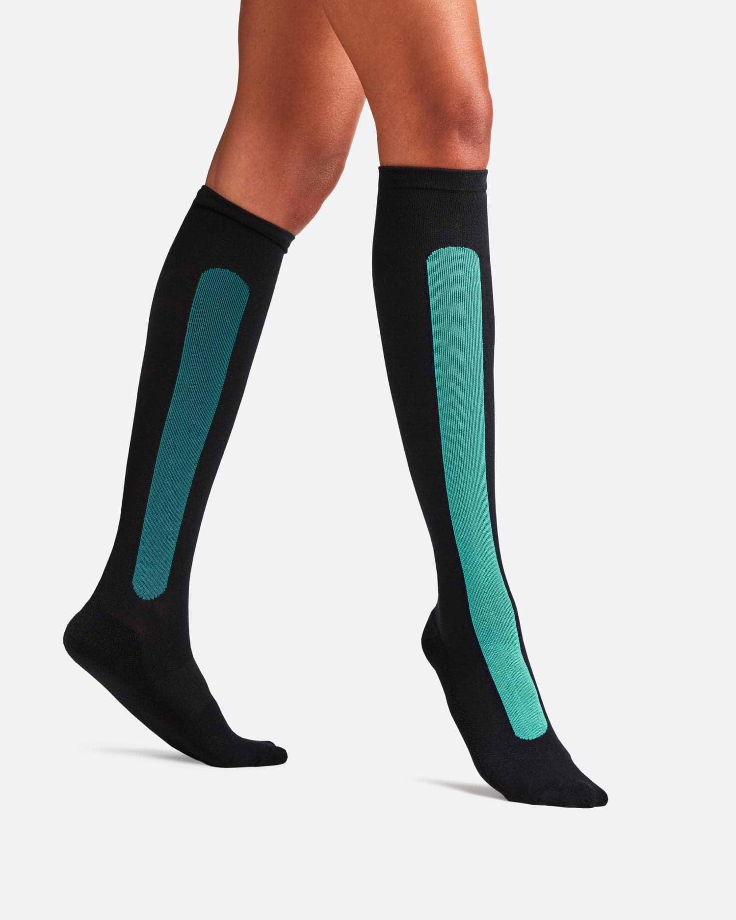 Side-profile view of a person walking, wearing knee-high Bamboo Compression Socks in the black and teal Blue Reef Caribbean Green colorway.