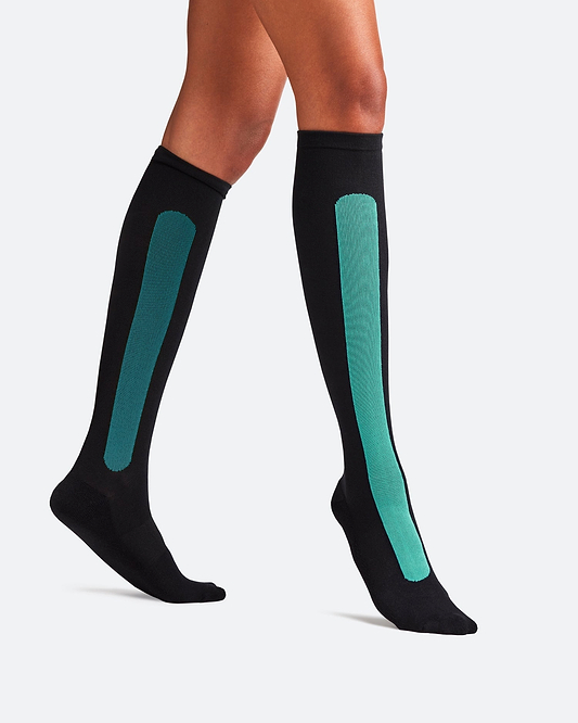 Side-profile view of a person walking, wearing knee-high Bamboo Compression Socks in the black and teal Blue Reef Caribbean Green colorway.