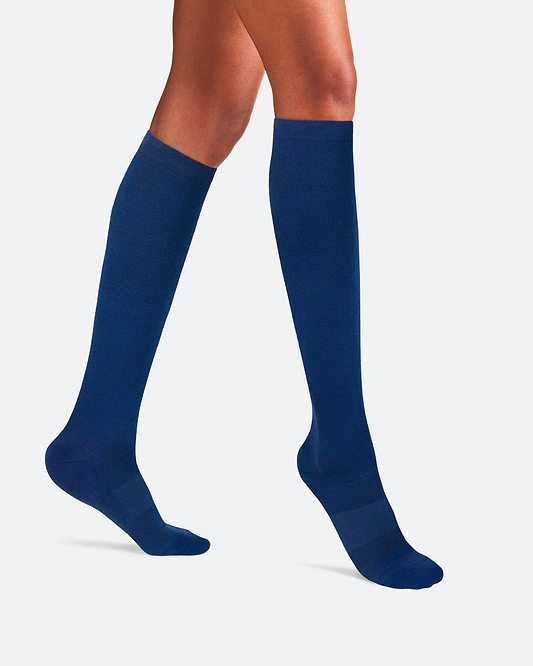 Side-profile view of a person's legs walking, wearing knee-high Ostrichpillow Bamboo Compression Socks in solid Seaside Siesta deep navy blue.