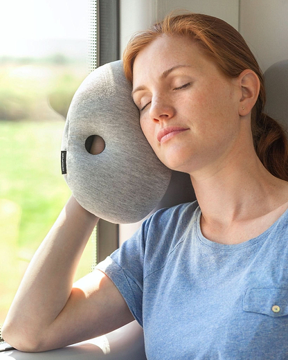 Woman resting on a train using the  Ostrichpillow Mini Handy Pillow