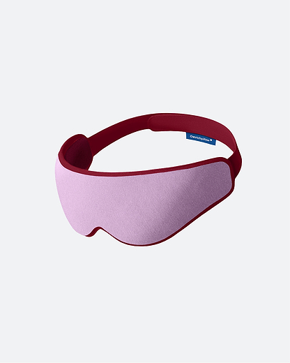 The Eye Mask in the color Dusk. The ergonomic sleep mask features a soft pink front panel framed by a burgundy border.