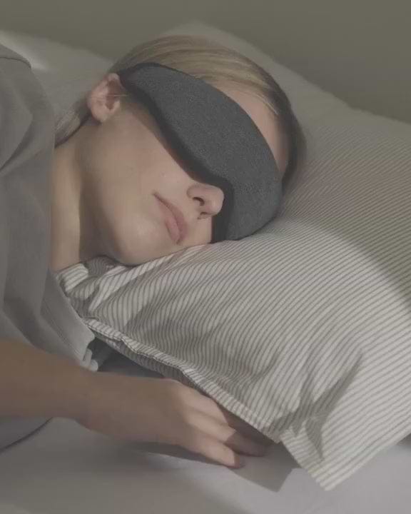 A woman rests with a dark grey Eye Mask. She smiles and text appears on screen that reads: 'Wake up refreshed'.