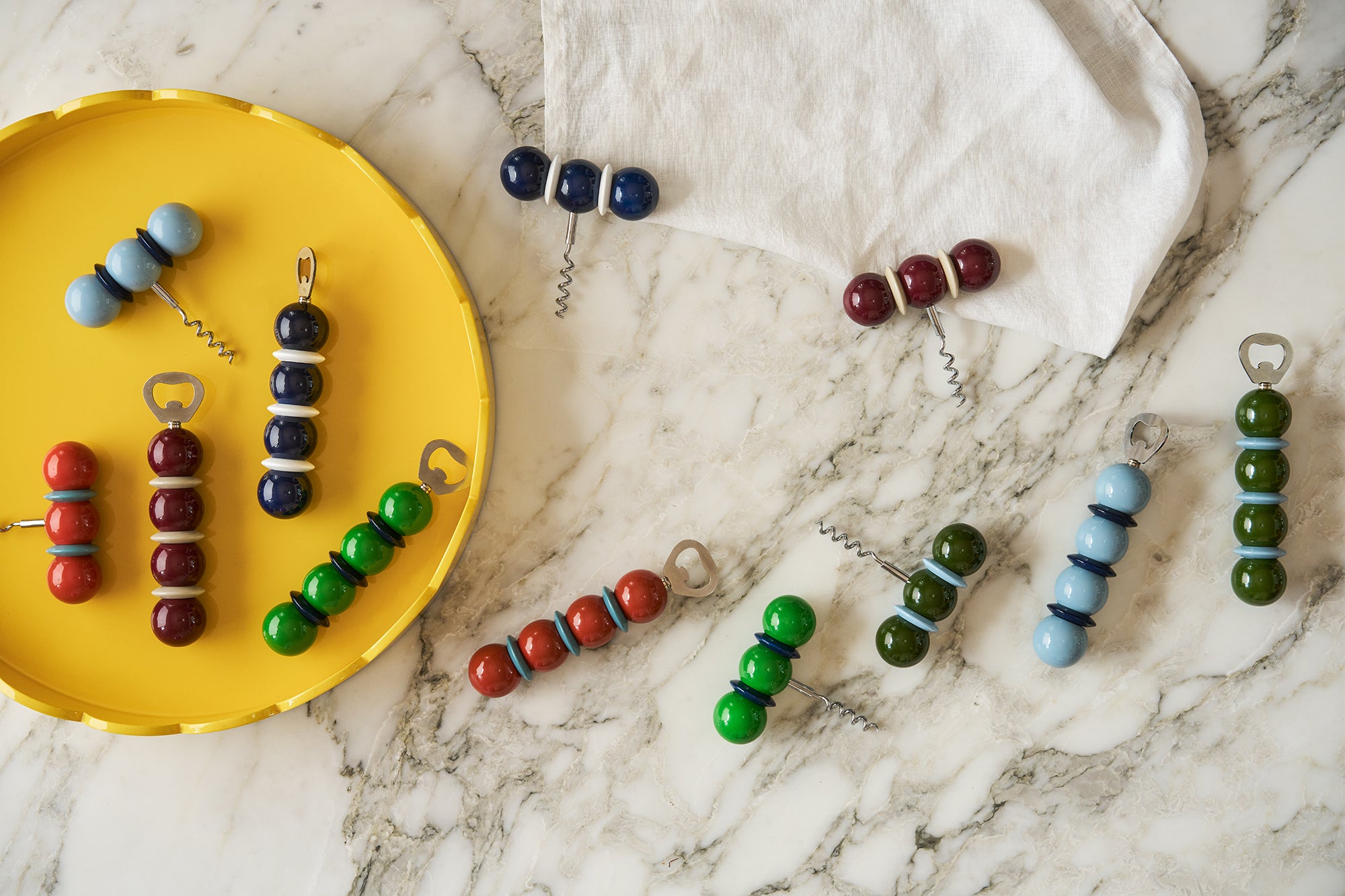 Addison Ross ball corkscrews and bottle openers in navy, red, green, light blue and burgundy laid out on marble