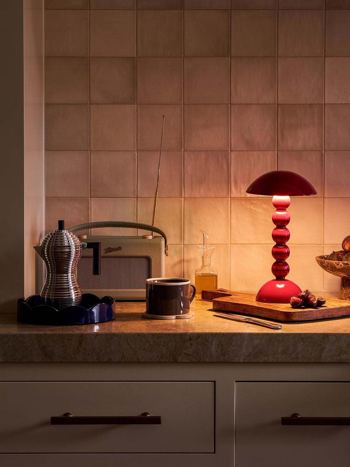 Addison Ross red Bobbin Lamp glowing on a kitchen counter beside coffee, figs and a vintage radio