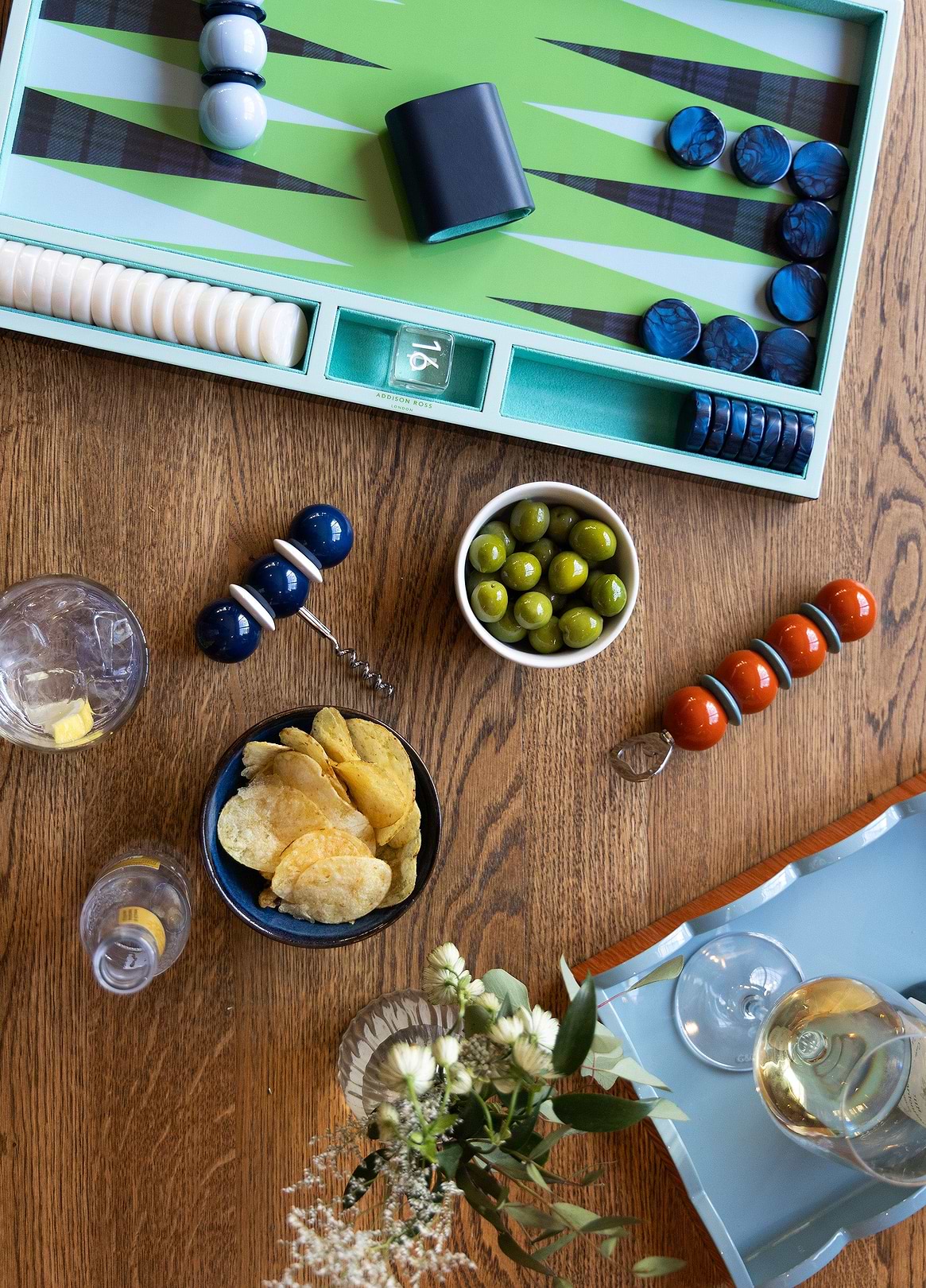 Overhead view of a styled home bar with backgammon set, olives, crisps and Addison Ross ball corkscrews