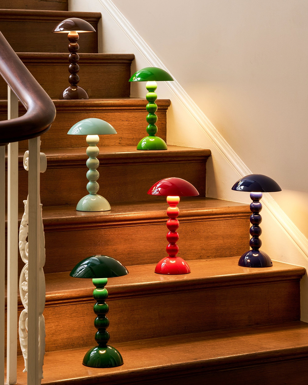 A set of colorful mushroom-shaped table lamps displayed on wooden stairs in a home interior setting.