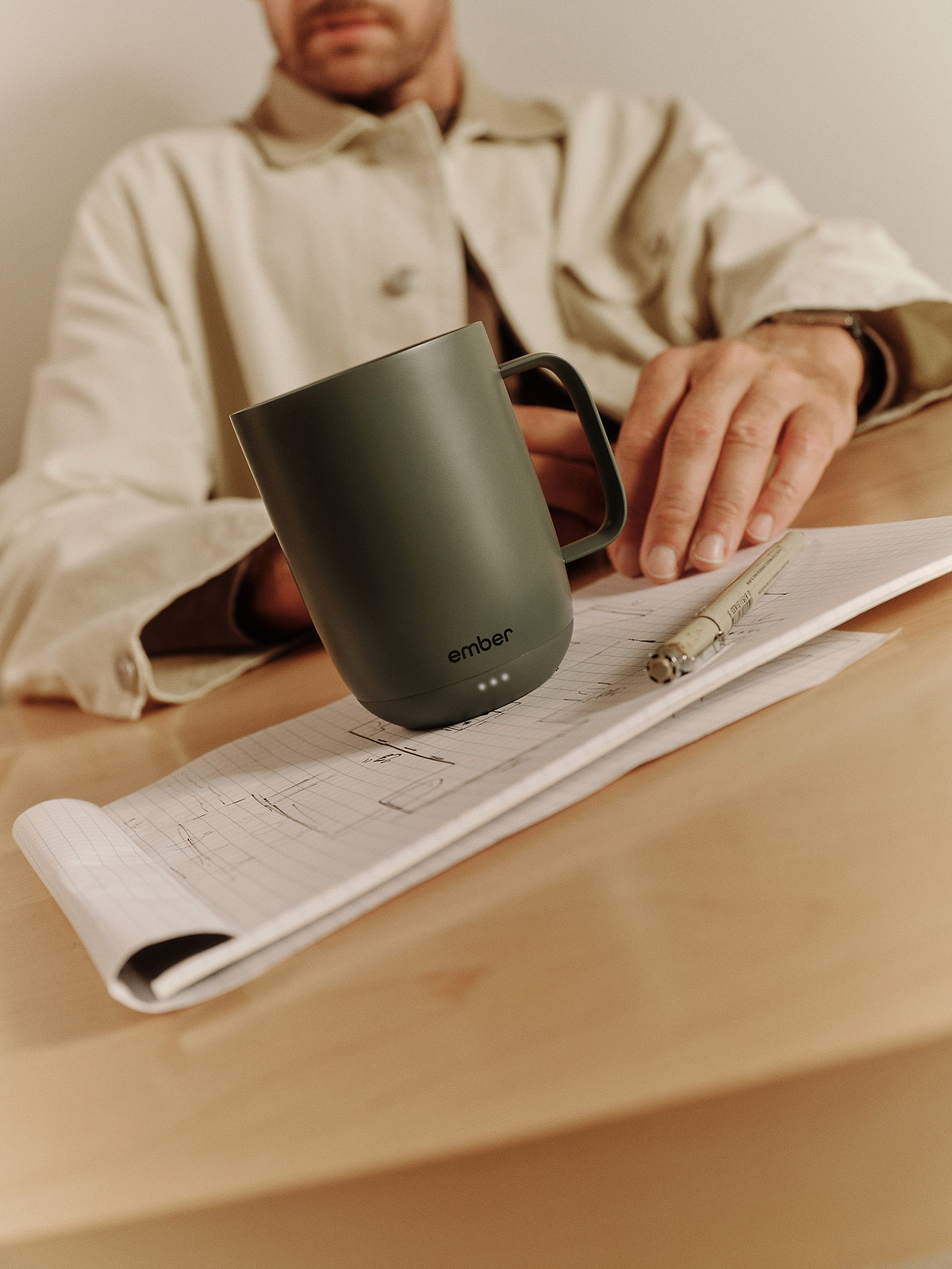 Sage green Ember Mug 3 with its indicator lights visible beside a notebook