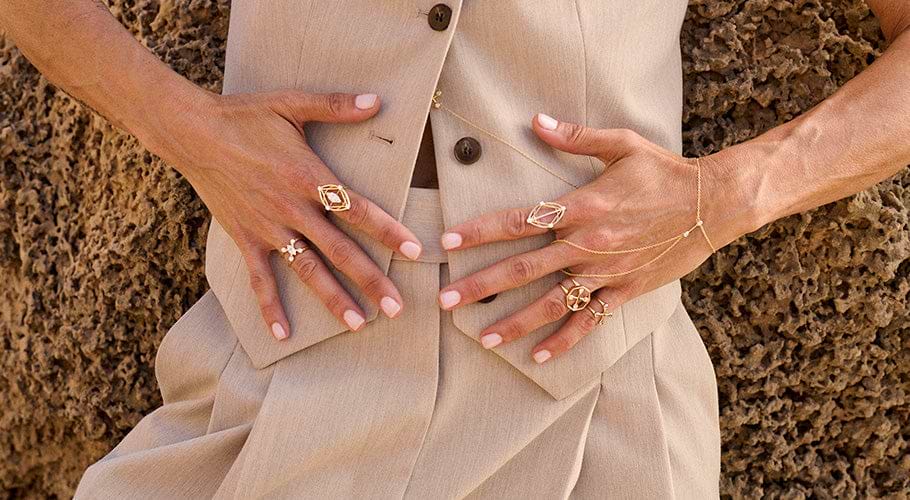 Hands wearing multiple ANNOORY gold rings and body chain jewelry