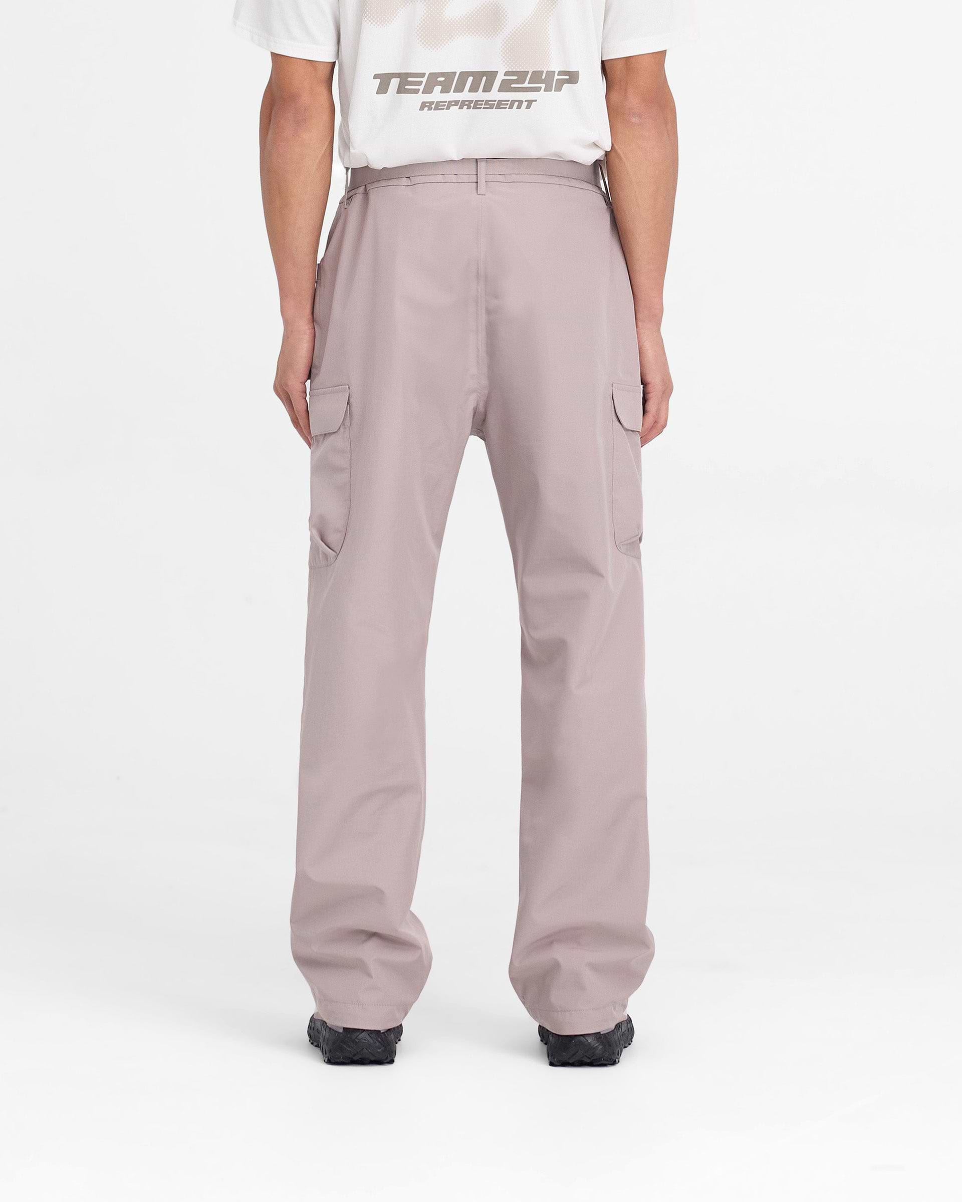 Man wearing grey technical cargo pants on a plain white background | 247 Technical Cargo Pant in Moonrock | Showerproof cargos with maglock buckle and bungee cord hem | 247 Pants | Represent Clo