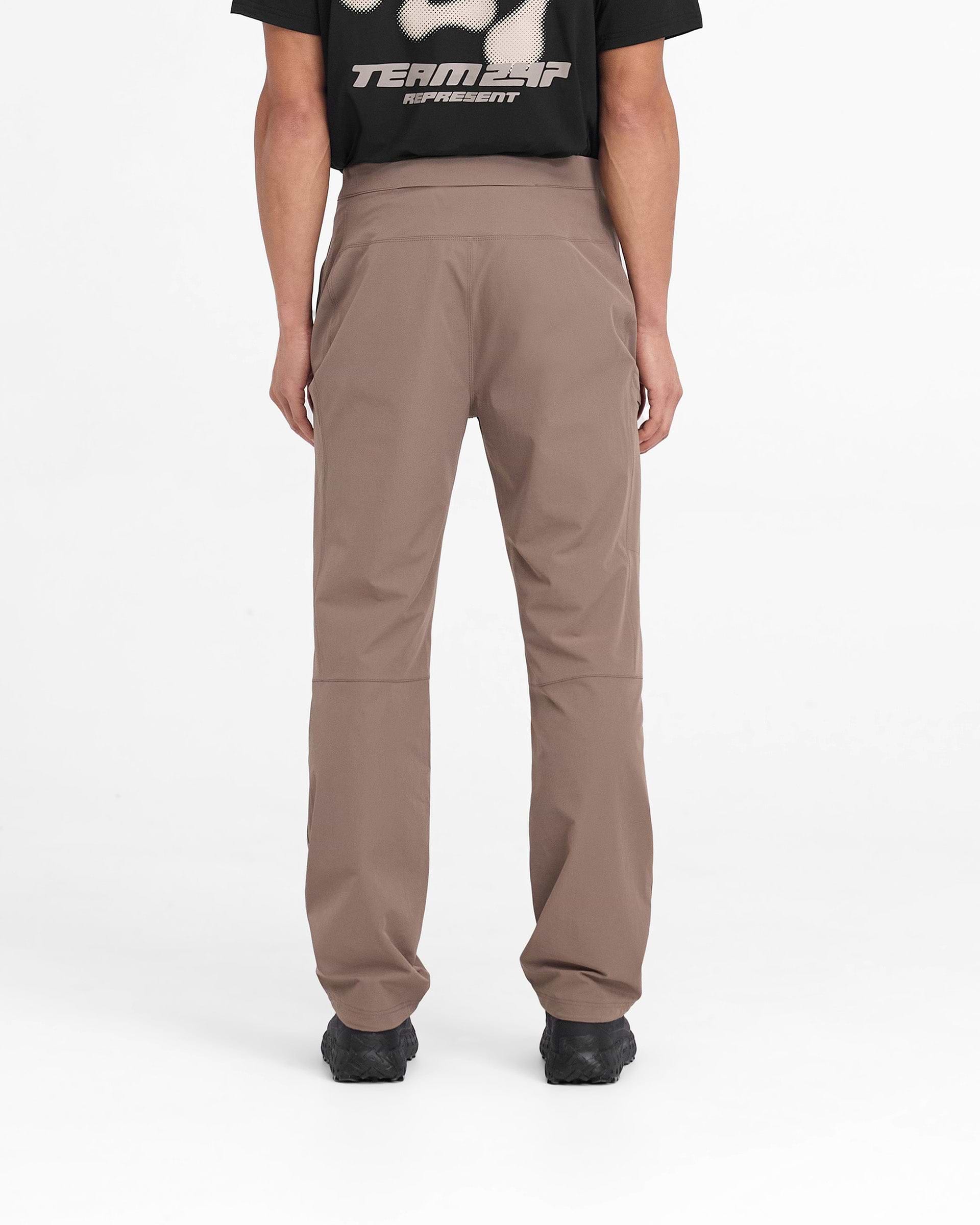 Man wearing umber pants on a plain white background | 247 Mission Pant in Umber | Nylon stretch pants with built-in belt and zip pockets | 247 Pants | Represent Clo