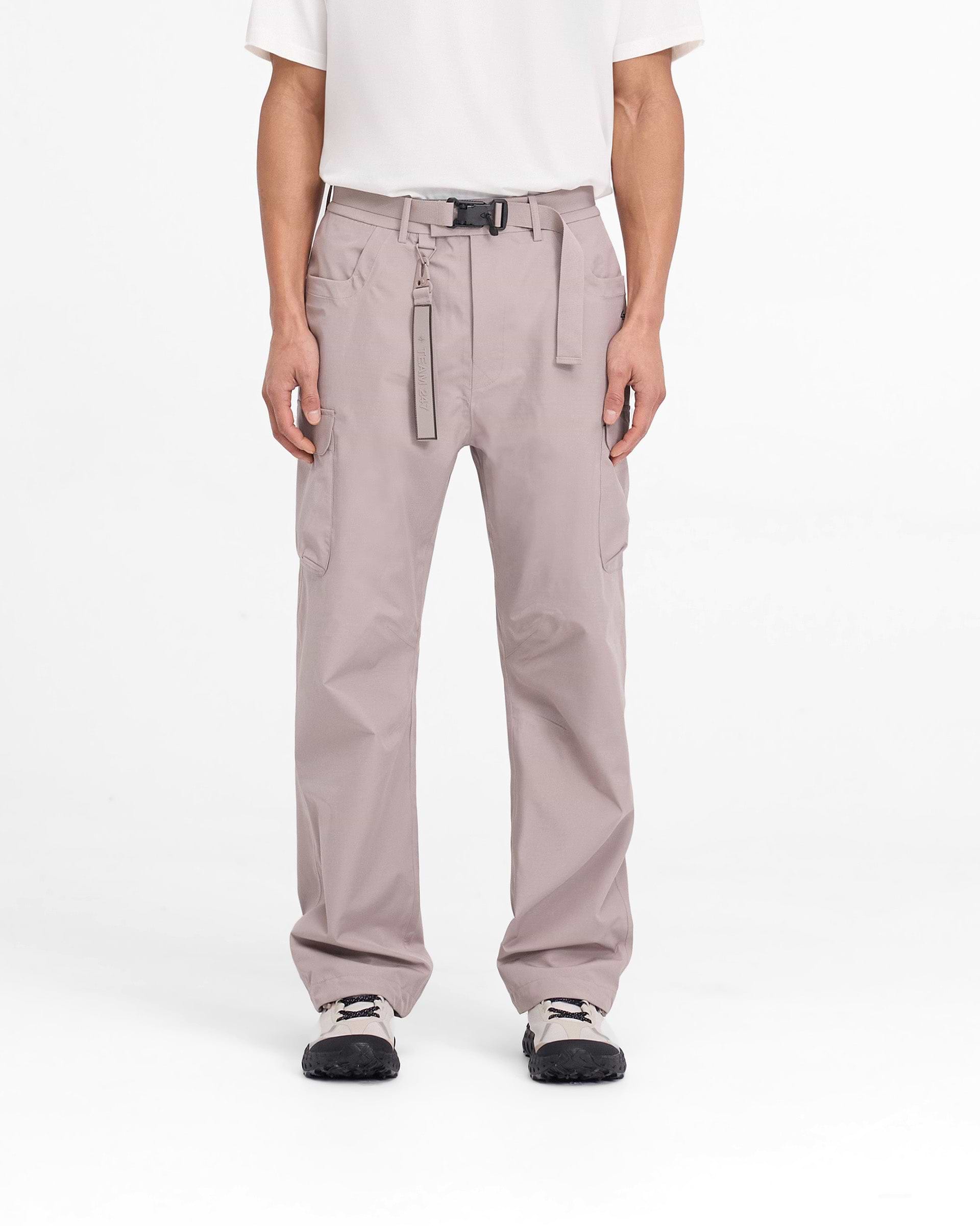 Man wearing grey technical cargo pants on a plain white background | 247 Technical Cargo Pant in Moonrock | Straight leg showerproof pants with maglock buckle and knee darts | 247 Pants | Represent Clo