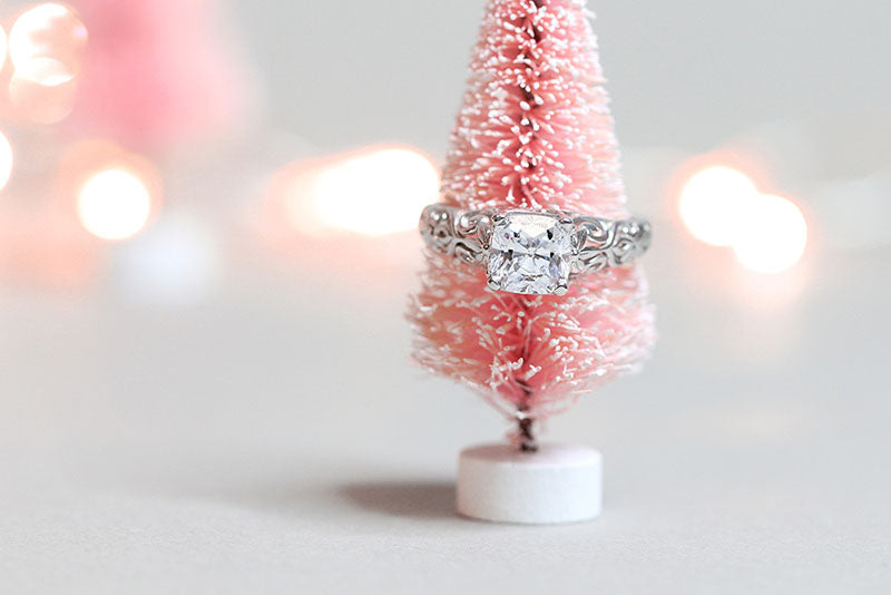 Affordable vintage and antique style solitaire engagement ring in 14k white gold posed on a cute snow dusted pink Christmas tree