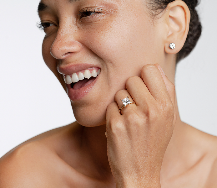 Woman wearing diamond earrings and ring on a white background