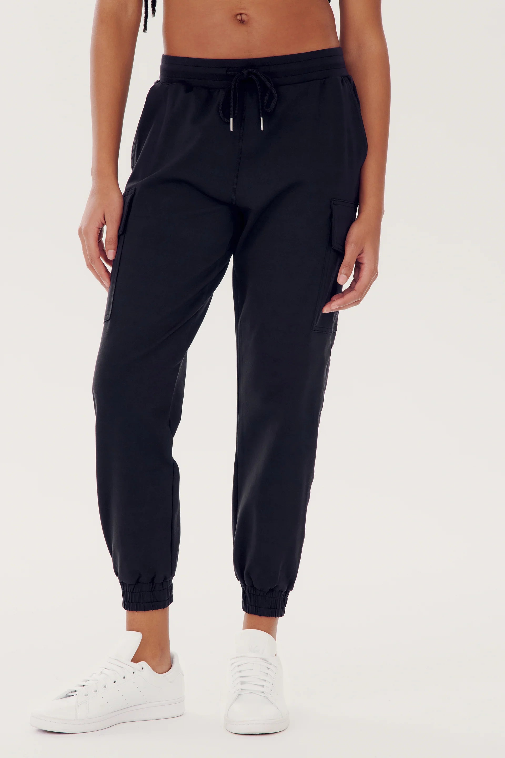 A person wearing black cargo jogger pants and white sneakers, standing against a plain light background.