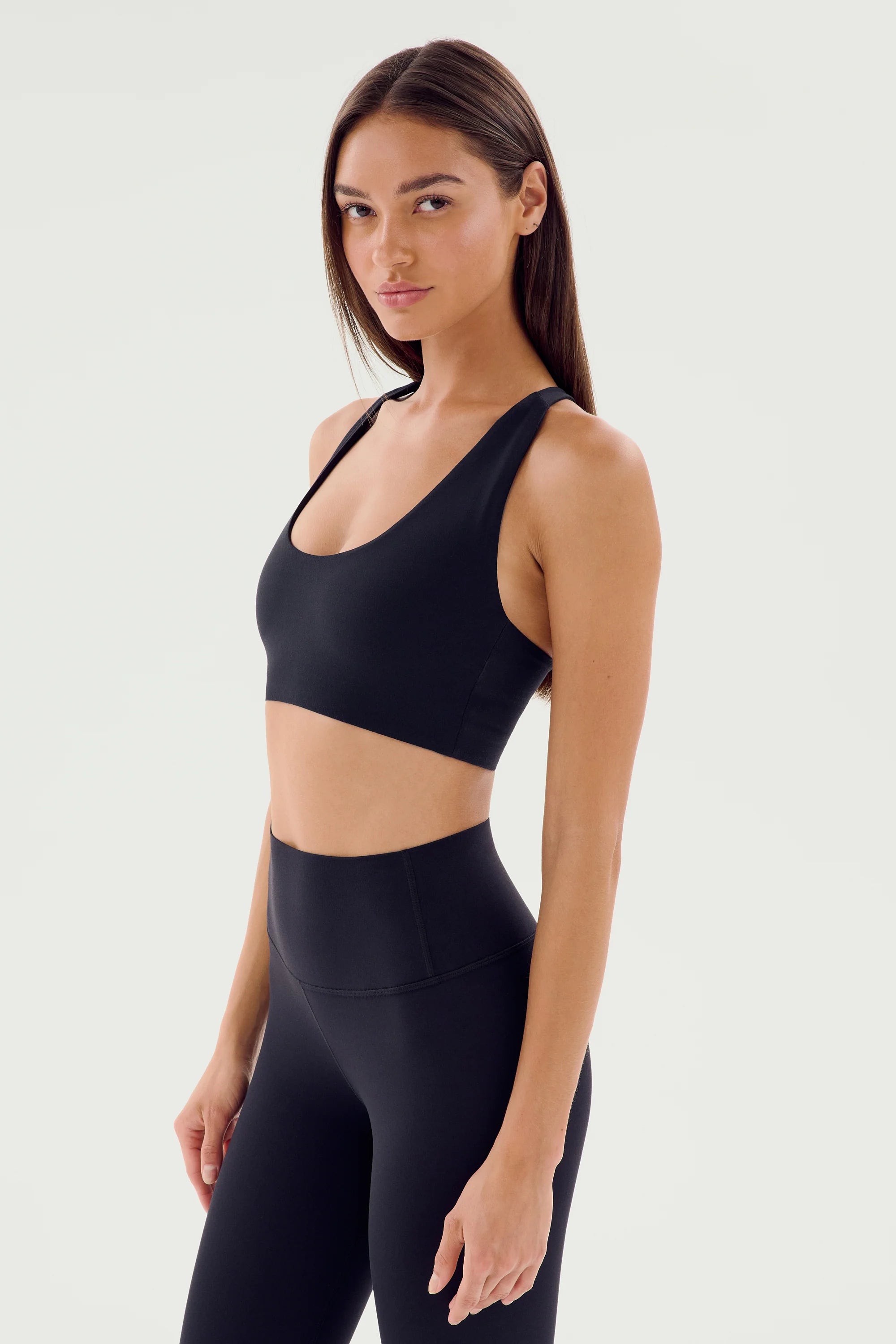A woman wearing a black sports bra and black high-waisted leggings poses against a plain white background.
