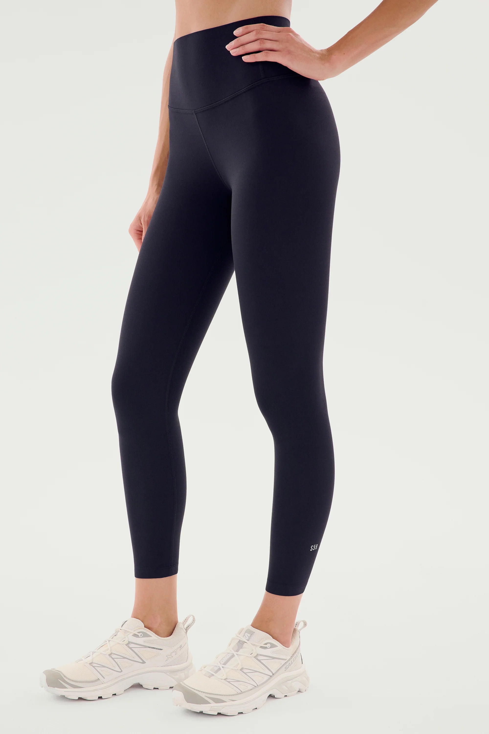 A person wearing high-waisted black leggings and white athletic shoes, posing against a plain light background.
