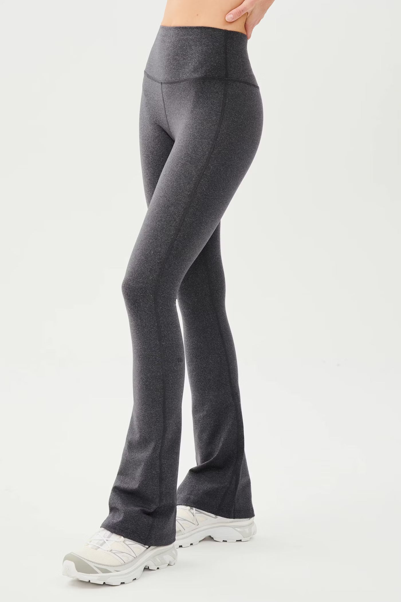 Person wearing high-waisted, dark gray flared leggings and white sneakers, standing against a plain white background.
