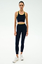 A person stands facing forward, wearing the SPLITS59 Amber Airweight Bralette in Indigo/Ray and matching leggings, made from Airweight performance fabric, paired with white sneakers against a plain light background.