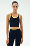 A woman stands against a plain background wearing the SPLITS59 Amber Airweight Bralette in Indigo/Ray, featuring a cropped scoop-neck style in performance fabric with yellow trim, looking directly at the camera.