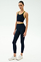 A woman wears the SPLITS59 Amber Airweight Bralette in Indigo/Ray with matching leggings and white sneakers, all crafted from Airweight performance fabric—ideal for hot yoga—posed against a plain white background.