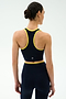 A woman faces away, wearing the SPLITS59 Amber Airweight Bralette in Indigo/Ray—an athletic crop top with yellow trim—paired with matching leggings, all made from Airweight performance fabric, set against a plain light background.