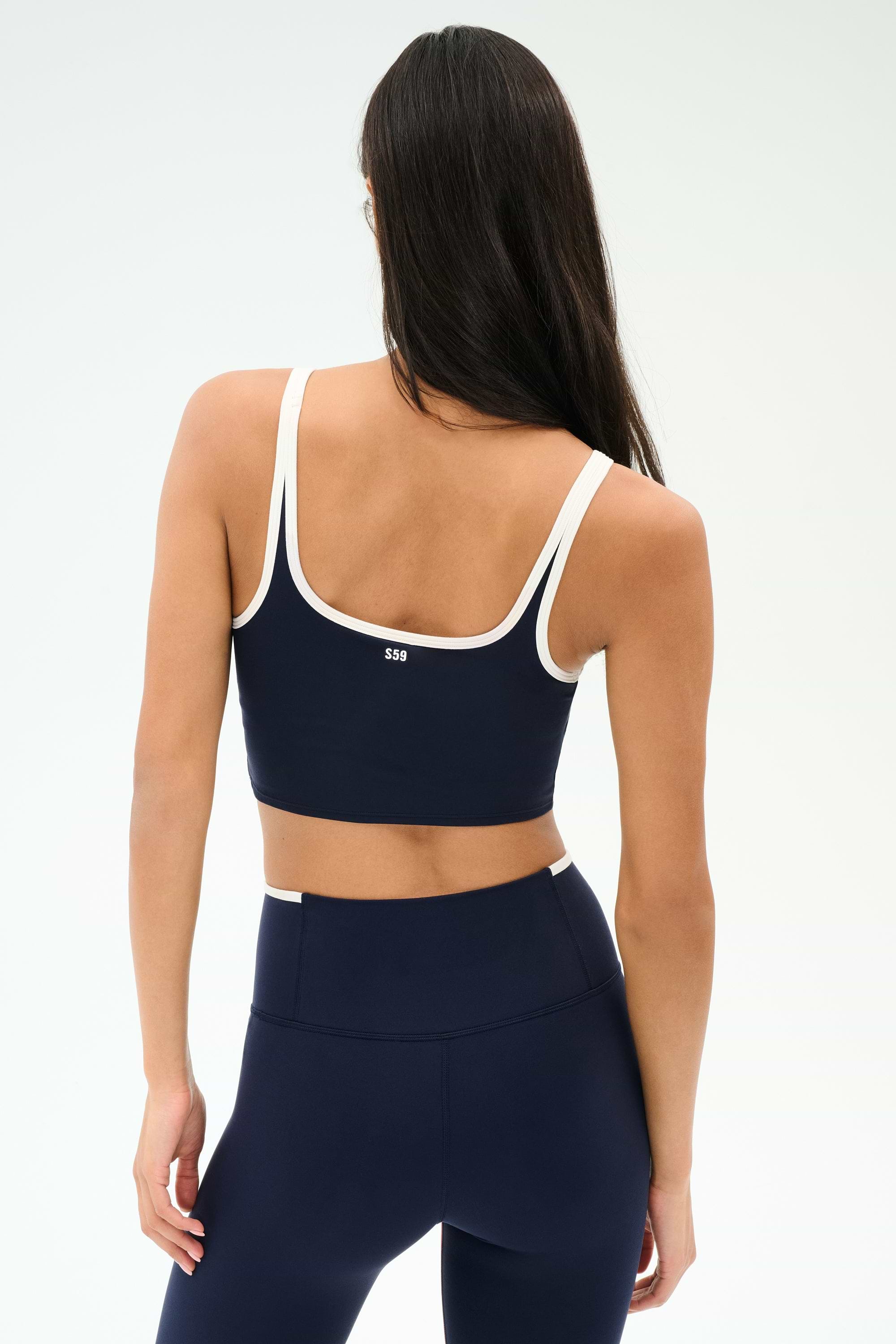 A woman is shown from the back wearing the SPLITS59 Cait Rigor Bralette in Indigo/White, paired with matching high-waisted leggings, both crafted from a soft nylon-spandex blend, against a plain background.