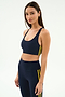 A woman models the SPLITS59 Ella Airweight Bra in Indigo/Bright Yellow, paired with matching leggings, highlighting the comfort and flexibility of its stretch fabric against a plain white background.