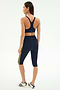 A woman stands facing away, wearing the SPLITS59 Ella Airweight Bra in Indigo/Bright Yellow and matching capri leggings, paired with white sneakers with black stripes, set against a plain background for an activewear look.