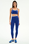 A woman faces forward in the SPLITS59 Elliah Airweight Double Layer Bra in Cobalt/White, paired with matching leggings and blue Adidas sneakers, against a plain white background.
