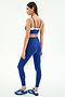 A woman stands in a studio wearing the SPLITS59 Dual High Waist Airweight 7/8 in Cobalt/White, a matching blue sports bra and high waist legging set with contrast waistband, perfect for hot yoga, paired with blue athletic shoes.